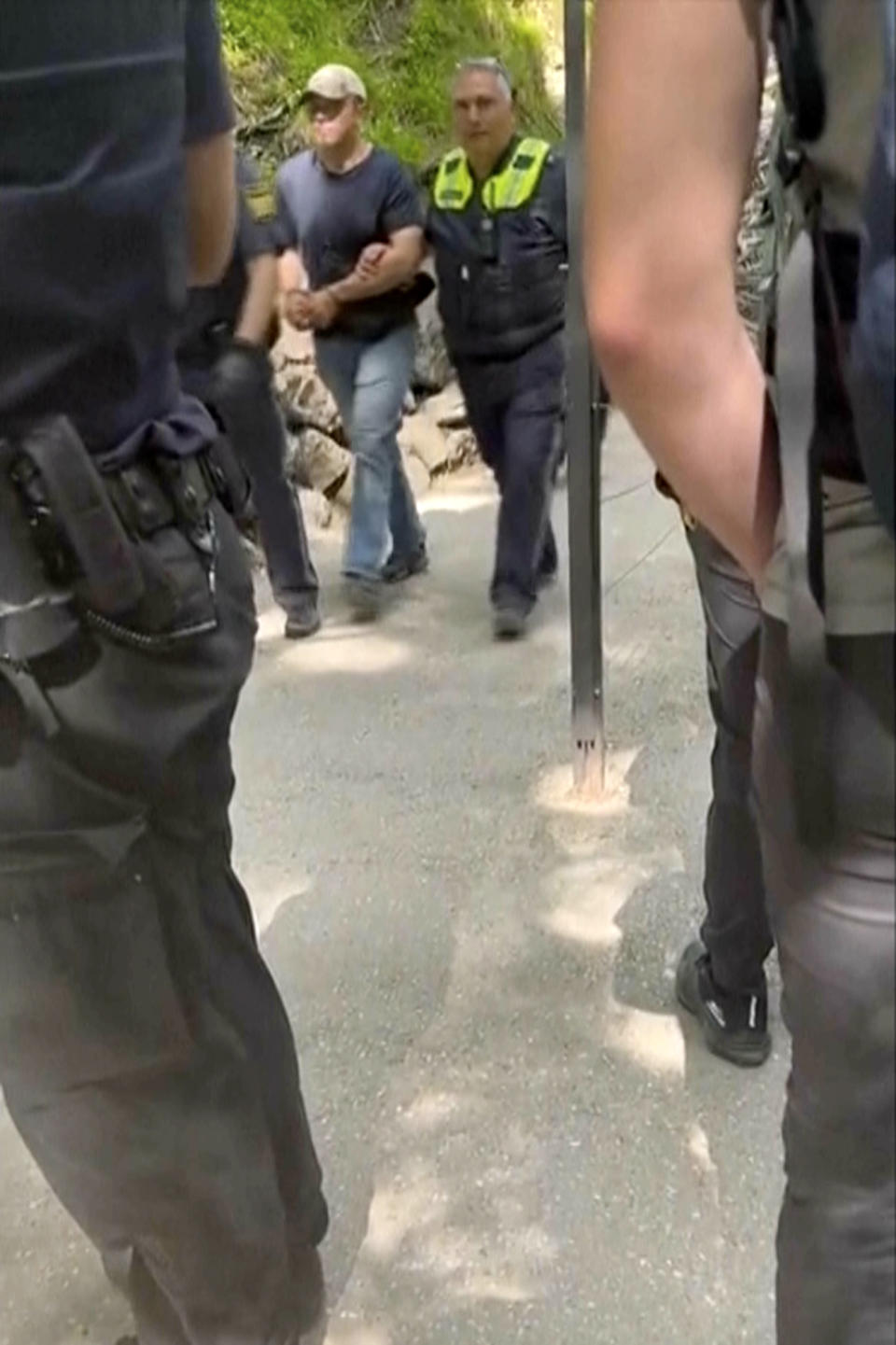 In this image taken from video, a suspect is taken away by two police officers near Neuschwanstein castle in Schwangau, southern Germany, Thursday June 15, 2023. An American man has been arrested after allegedly assaulting two U.S. tourists near Neuschwanstein castle in southern Germany and then pushing them down a steep slope, an attack that left one of the women dead, authorities said Thursday. (Eric Abneri via AP)