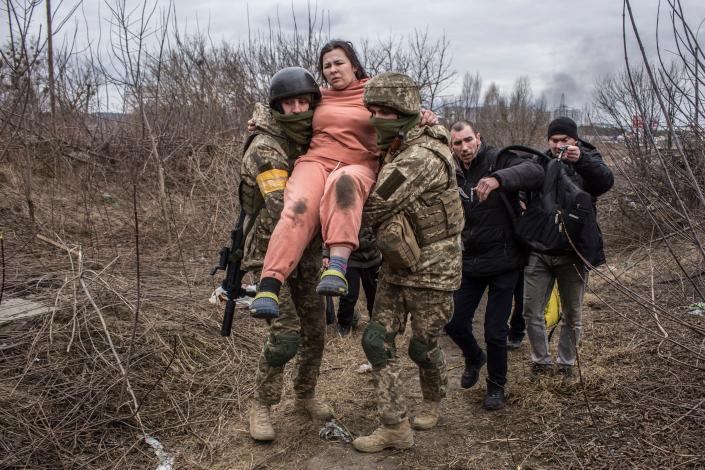 A woman carried by Ukrainian soldiers crosses an improvised path while fleeing the town of Irpin, Ukraine on Sunday, March 6. In Irpin, near Kyiv, a sea of people on foot and even in wheelbarrows trudged over the remains of a destroyed bridge to cross a river and leave the city.