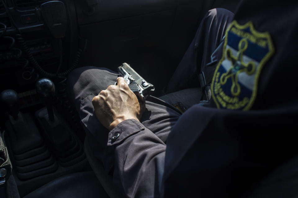 In this April 14, 2014 photo, a police officer holds his service weapon by his lap while patrolling in a neighborhood controlled by the Mara Salvatrucha gang in Ilopango, El Salvador. Public Safety Minister Ricardo Perdomo said the gangs have also increased their attacks against police. He said members of the Mara 18 gang have orders to take revenge police and soldiers who wound or kill one of their own. (AP Photo/Salvador Melendez)