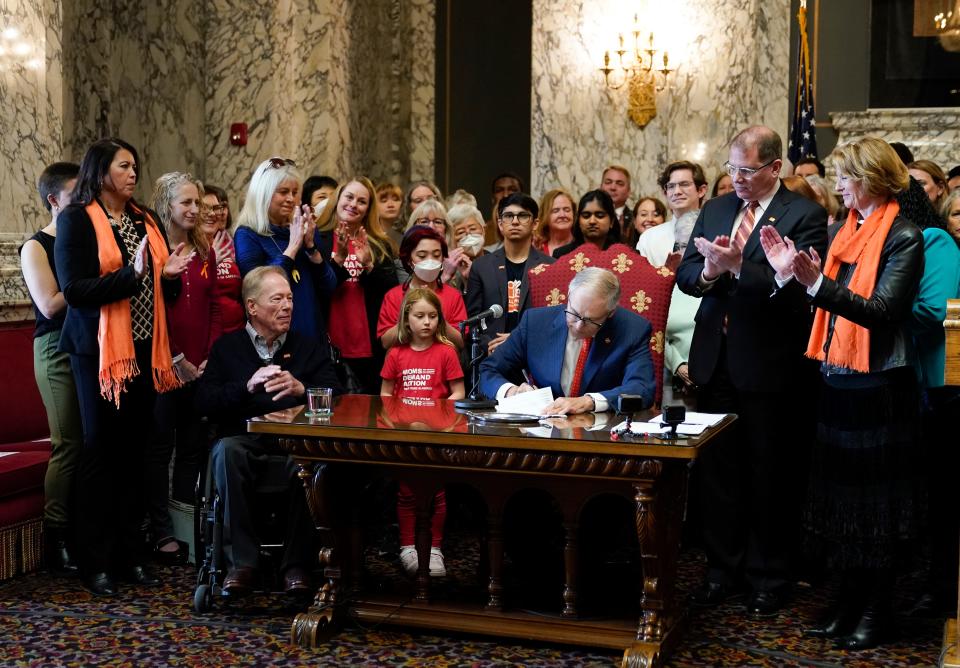 people gather around a man signing a bill into law on a desk