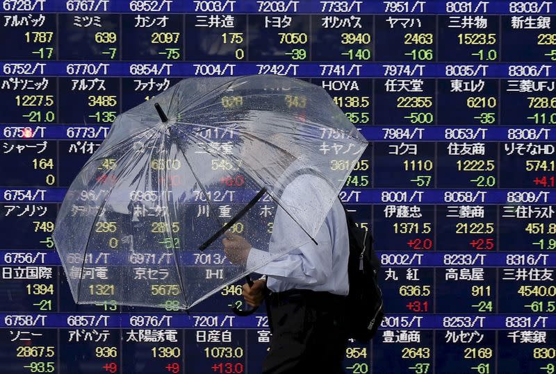 A man holding an umbrella walks in front of an electronic stock quotation board outside a brokerage in Tokyo, in this September 8, 2015 file photo. REUTERS/Issei Kato/Files