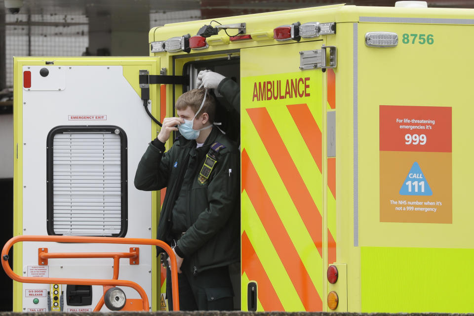 FILE - In this Tuesday, March 31, 2020 a paramedic is assisted in putting on a mask at St Thomas' Hospital, one of the many hospitals dealing with coronavirus patients in London. Britain's National Health Service, cornerstone of the nation's post-war welfare state, may be stretched to the breaking point in coming weeks as hospitals brace for an expected tsunami of critically ill patients when the coronavirus pandemic reaches its peak across the United Kingdom. (AP Photo/Kirsty Wigglesworth, File)