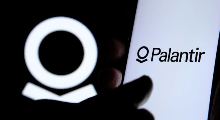 A close-up shot of a hand and the Palantir (PLTR) logo.