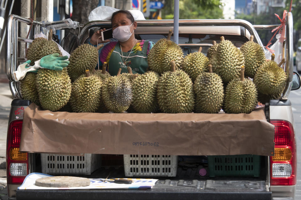 A fruit vendor wearing a face mask to protect from the new coronavirus talks on a mobile phone near durian on her van in Bangkok, Thailand, Thursday, April 23, 2020. A month-long state of emergency remain enforced in Thailand to allow its government to impose stricter measures to control the coronavirus that has infected hundreds of people in the Southeast Asian country. (AP Photo/Sakchai Lalit)