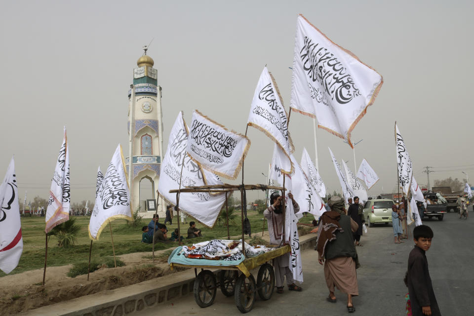 An Afghan man and children sell Taliban flags on a street during a celebration marking the second anniversary of the withdrawal of U.S.-led troops from Afghanistan, in Kandahar, south of Kabul, Afghanistan, Tuesday, Aug. 15, 2023. (AP Photo/Abdul Khaliq)