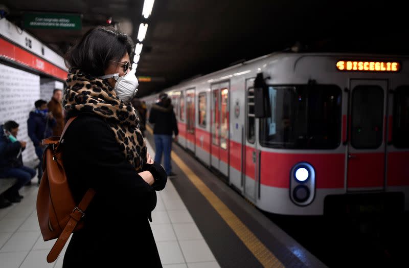 A woman wearing a face mask waits at a metro platform in Milan