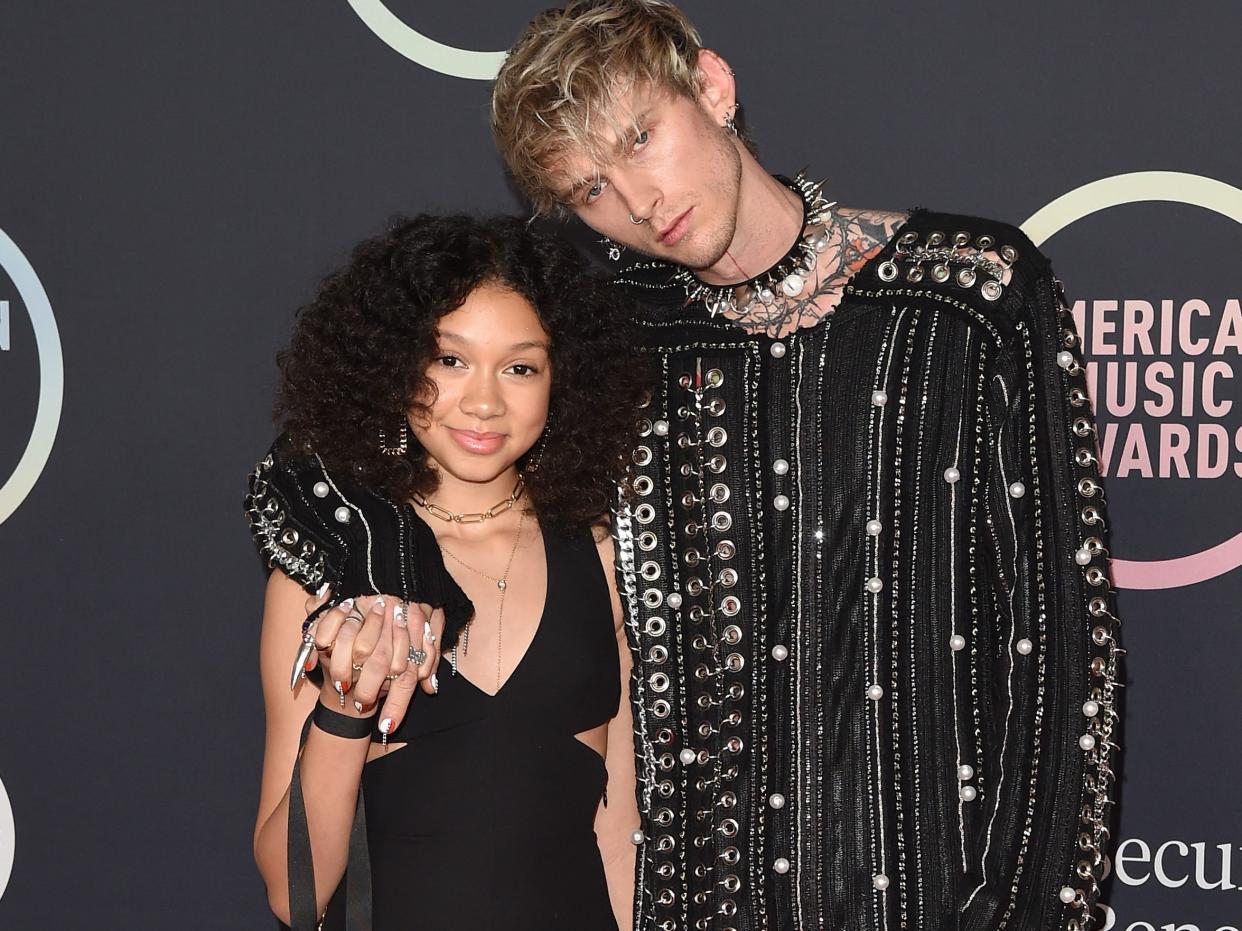 Casie Colson Baker, in a black gown, and Machine Gun Kelly, in black pants, and a black metallic top, pose for photos on the red carpet in 2021.