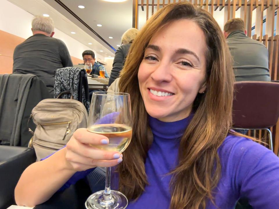 The writer wears a purple turtleneck and holds a glass of wine while sitting in the Delta Sky Club lounge