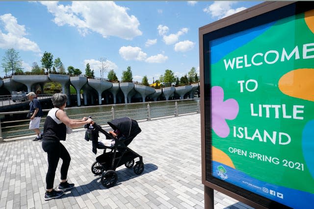 A woman rolls a baby carriage past a series of concrete tulip pots that support Little Island in New York