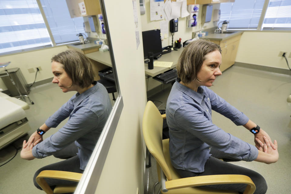 Jennifer Haller is reflected in a mirror as she waits in an exam room before she was given a shot in the first-stage safety study clinical trial of a potential coronavirus vaccine, Monday, March 16, 2020, at the Kaiser Permanente Washington Health Research Institute in Seattle. Haller was the first person to receive the shot in the study. (AP Photo/Ted S. Warren)