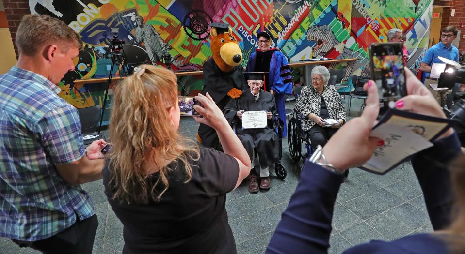 Robert Greathouse, center, poses for photographs Monday with his degree after a ceremony at the University of Akron's College of Arts and Sciences.