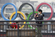 People wearing face masks to protect against the spread of the coronavirus stand at the Odaiba waterfront as Olympic rings is seen in the background in Tokyo, Tuesday, Jan. 26, 2021. (AP Photo/Koji Sasahara)