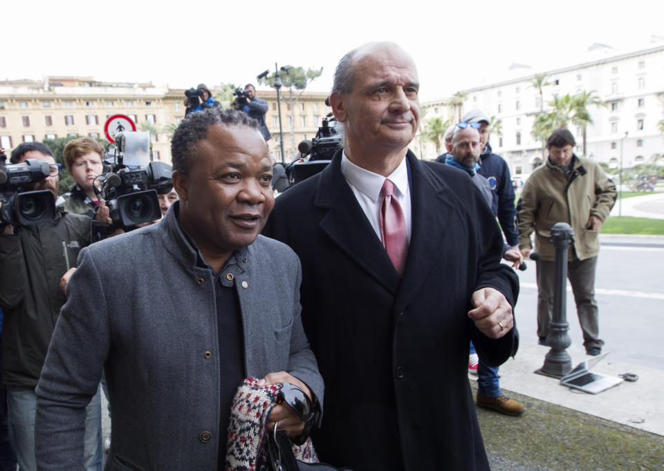 FILE- Diya "Patrick" Lumumba, left, a Congolese citizen who was originally jailed for the murder of Meredith Kercher, flanked by his lawyer Carlo Pacelli, arrives at the Italy's highest court building, in Rome, Friday, March 27, 2015. Amanda Knox faces yet another trial for slander against Lumumba in a case that could remove the last remaining guilty verdict against her eight years after Italy's highest court definitively threw out her conviction for the murder of her 21-year-old British roommate, Meredith Kercher. (AP Photo/Riccardo De Luca, File)