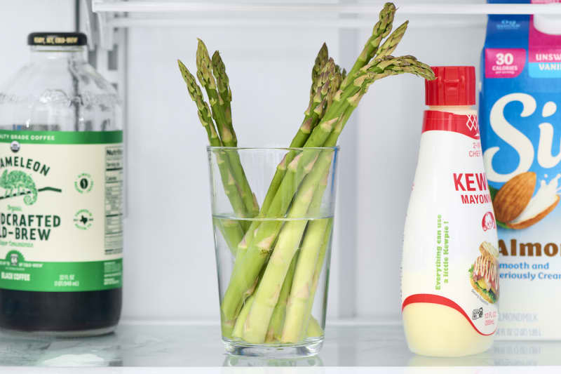 head on shot of asparagus in a glass of water in the fridge.