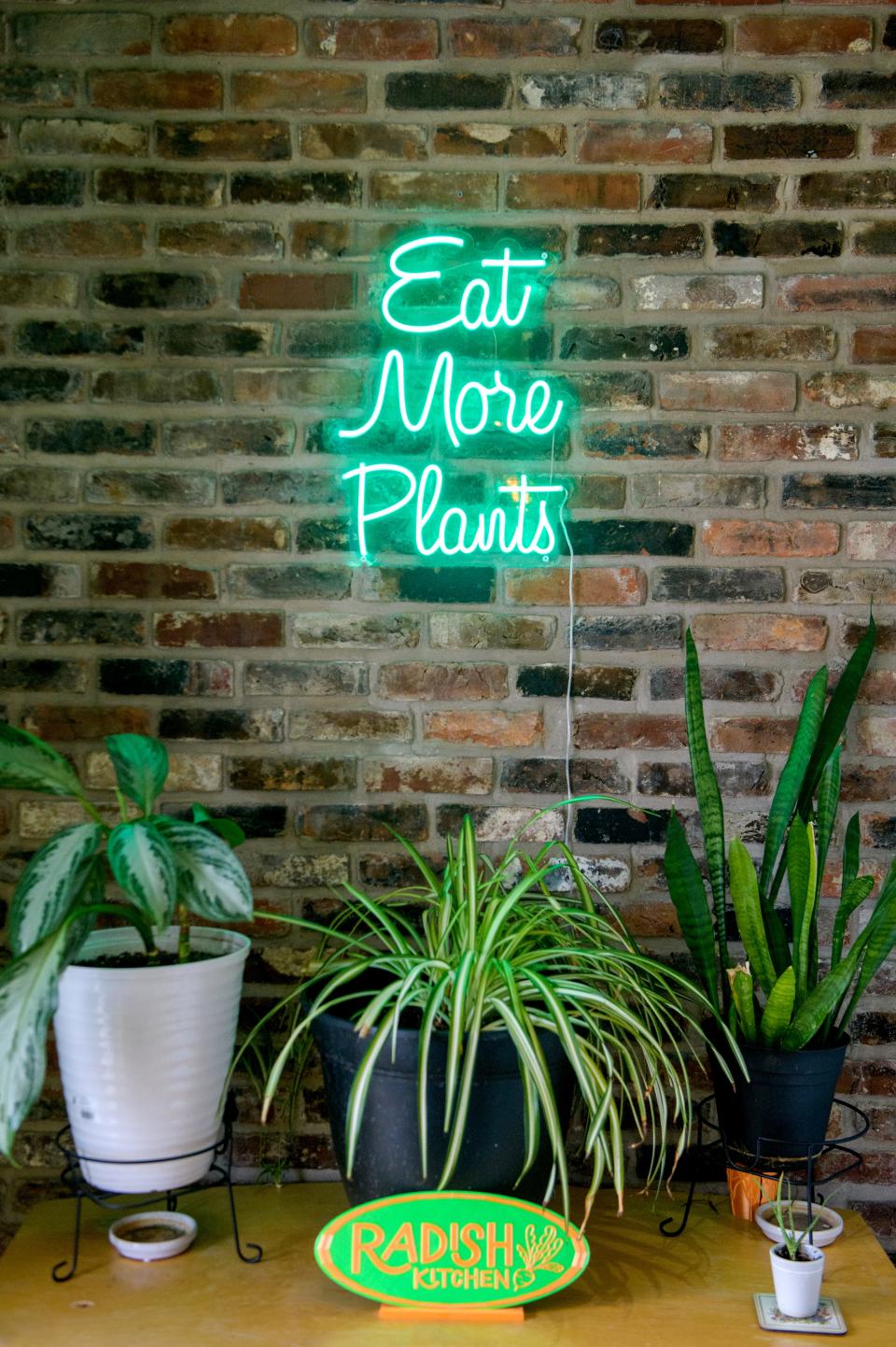 A neon sign declaring "Eat More Plants" decorates a wall at the entrance to Radish Kitchen in Campustown.