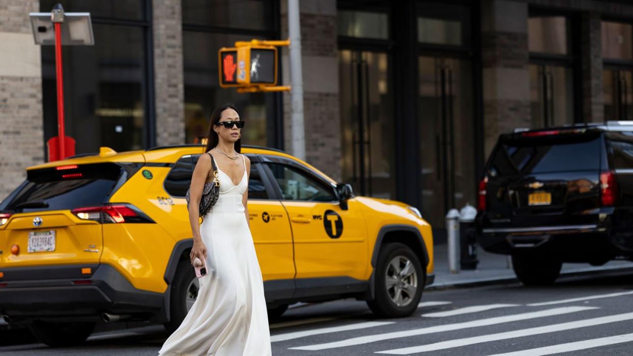 a person in a white dress and sunglasses standing in the middle of a street