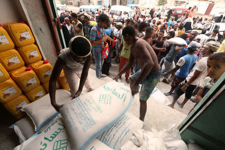 Workers unload sacks of wheat flour as people gather outside an aid distribution centre in the Red Sea port city of Hodeidah, Yemen June 14, 2018. REUTERS/Abduljabbar Zeyad