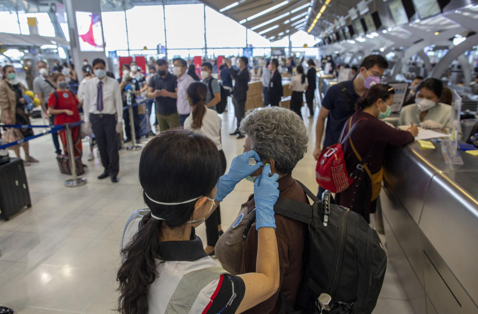 A health worker checks the temperature of a tourist from Wuhan, China, as she waits for a charter flight back to Wuhan at the Suvarnabhumi airport, Bangkok, Thailand, Friday, Jan. 31, 2020. A group of Chinese tourists who have been trapped in Thailand since Wuhan was locked down due to an outbreak of new virus returned to China on Friday. (AP Photo/Gemunu Amarasinghe)