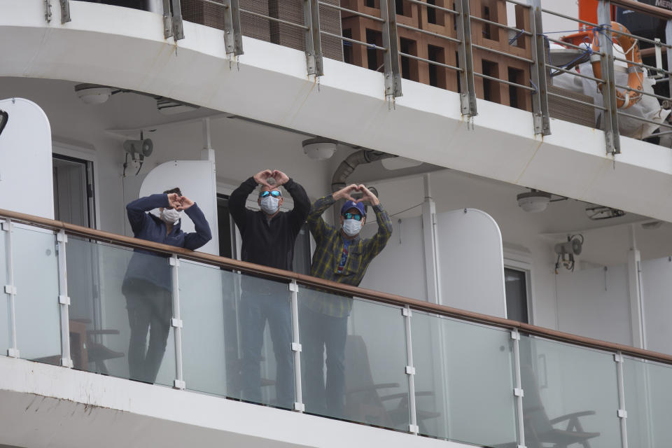 Passengers on the Australian cruise ship name Greg Mortimer gesture heart signs as they arrive to port on their way to the international airport in Montevideo, Uruguay, Wednesday, April 15, 2020. The ship has been anchored off Uruguay's coast since March 27 with more than half its passengers and crew infected with the new coronavirus, according to authorities. (AP Photo/Matilde Campodonico)