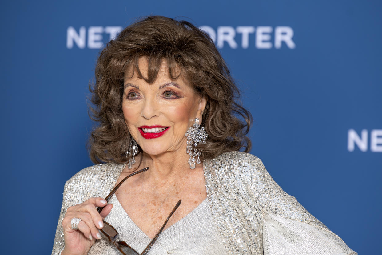 Joan Collins, wearing a silver dress and sequinned cape, with large dangling diamond earrings and holding a pair of sunglasses in one hand, arrives at the V&A 2023 Summer Party at The V&A