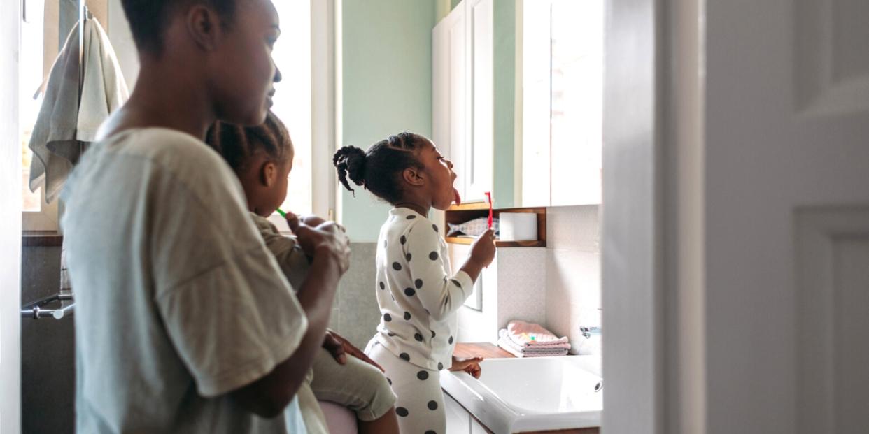 mom helping daughters brush teeth in bathroom - intensive parenting