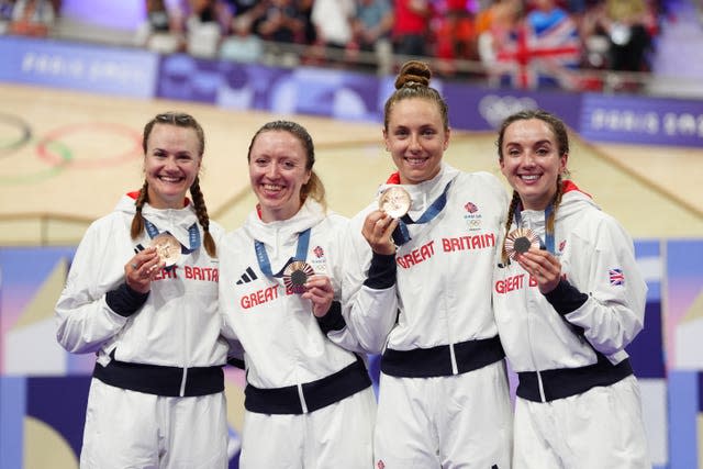 Four women in white tracksuits hold their medals