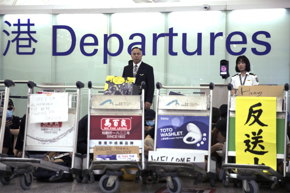 Airport security personnel look on as protesters using luggage trolleys to block the departure gates during a demonstration at the Airport in Hong Kong, Tuesday, Aug. 13, 2019. Protesters severely crippled operations at Hong Kong's international airport for a second day Tuesday, forcing authorities to cancel all remaining flights out of the city after demonstrators took over the terminals as part of their push for democratic reforms. (AP Photo/Vincent Thian)