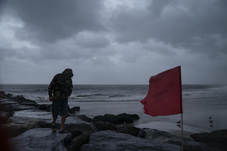 Storm clouds pass overhead as surfers enjoy the waves on a closed beach as Tropical Storm Henri brings strong surf and high winds to the area, Sunday, Aug. 22, 2021, in the Rockaways neighborhood of the Queens borough of New York. (AP Photo/John Minchillo)