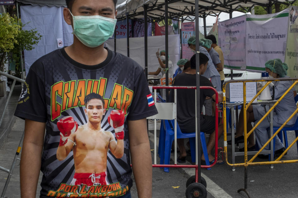 In this Thursday, March 19, 2020, photo, a Muay Thai boxing fighter stands in front of makeshift screening facility outside Rajadamnern boxing stadium in Bangkok, Thailand. Kickboxing aficionados came from all over Thailand to attend a major Muay Thai tournament at Bangkok's indoor Lumpini Stadium on March 6, 2020. Dozens or more went home unknowingly carrying the coronavirus. For most people the new COVID-19 coronavirus causes only mild or moderate symptoms, but for some it can cause more severe illness. (AP Photo/Gemunu Amarasinghe)