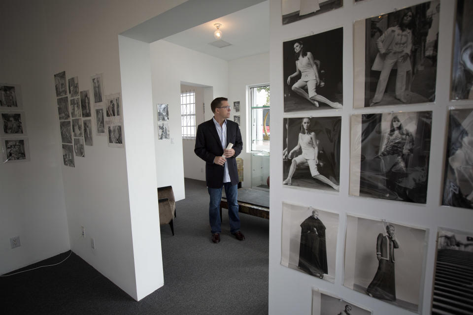 In this Monday, Dec. 30, 2013 photo, auctioneer Rico Baca stands beside some of some of the early fashion photos in West Palm Beach, Fla. The signature of designer Karl Lagerfeld is adding an extra splash of glamour to a collection of fashion sketches up for auction in Florida. The half-century-old archive from the House of Tiziani in Rome will be sold Jan. 11, 2014, at Palm Beach Modern Auctions. In the 1960s, Tiziani designed movie costumes and clothing for Elizabeth Taylor and other celebrities. (AP Photo/J Pat Carter)