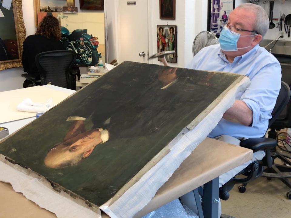 A painting being re-stretched onto a wooden frame.