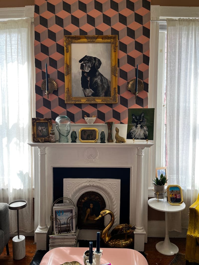 Dog portrait hung on graphic wall over art and decor atop white mantle in living room.