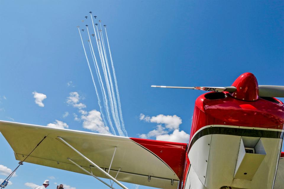 Planes streak above in the skies above a parked airplane during EAA AirVenture, Monday, July 25, 2022, in Oshkosh, Wis.