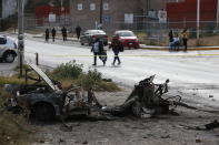 Locals walk past a burned-out car outside the Tula General Hospital, after a gang rammed several vehicles into a prison and escaped with nine inmates, in Tula, Mexico, Wednesday, Dec. 1, 2021. Local media reported that the burned-out cars found in the city after the attack were car bombs. Authorities said they were investigating how the vehicles caught fire. (AP Photo/Ginnette Riquelme)