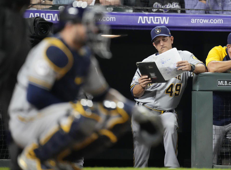 FILE - In this June 19, 2021, file photo, Milwaukee Brewers hitting coach Andy Haines studies notes while the Colorado Rockies bat during the seventh inning of a baseball game in Denver. Haines is out as the Milwaukee Brewers’ hitting coach after they scored a total of six runs in their four-game National League Division Series loss to the Atlanta Braves, the team announced Wednesday, Oct. 20, 2021. (AP Photo/David Zalubowski, File)