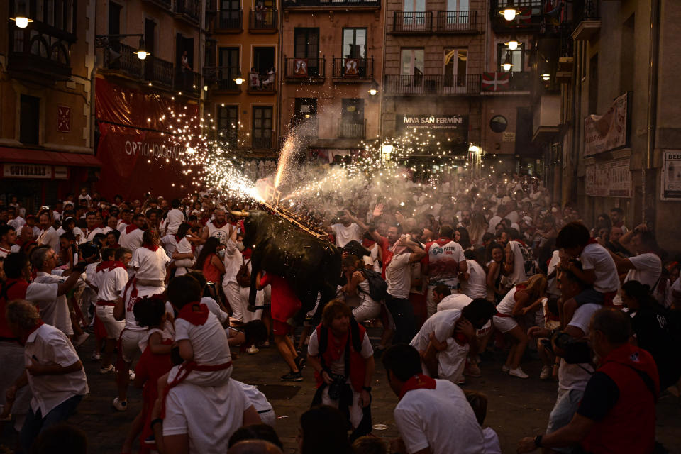 A man runs through the streets carrying a fake bull's head and horns that shoots out sparks in all directions, at the San Fermin Festival in Pamplona, northern Spain, Wednesday, July 13, 2022. (AP Photo/Alvaro Barrientos)