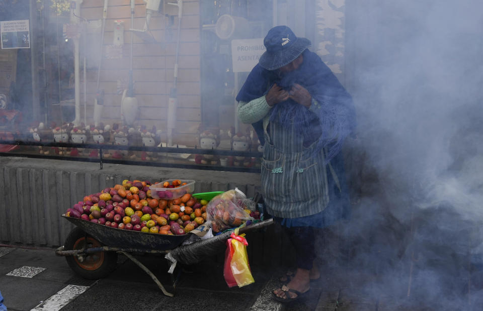 A fruit vendor covers her nose and mouth amid tear gas fired by police during clashes with protesting educators near the government palace in La Paz, Bolivia, Wednesday, April 12, 2023. Teachers are demanding higher pay and protesting the new curriculum at public schools. (AP Photo/Juan Karita)