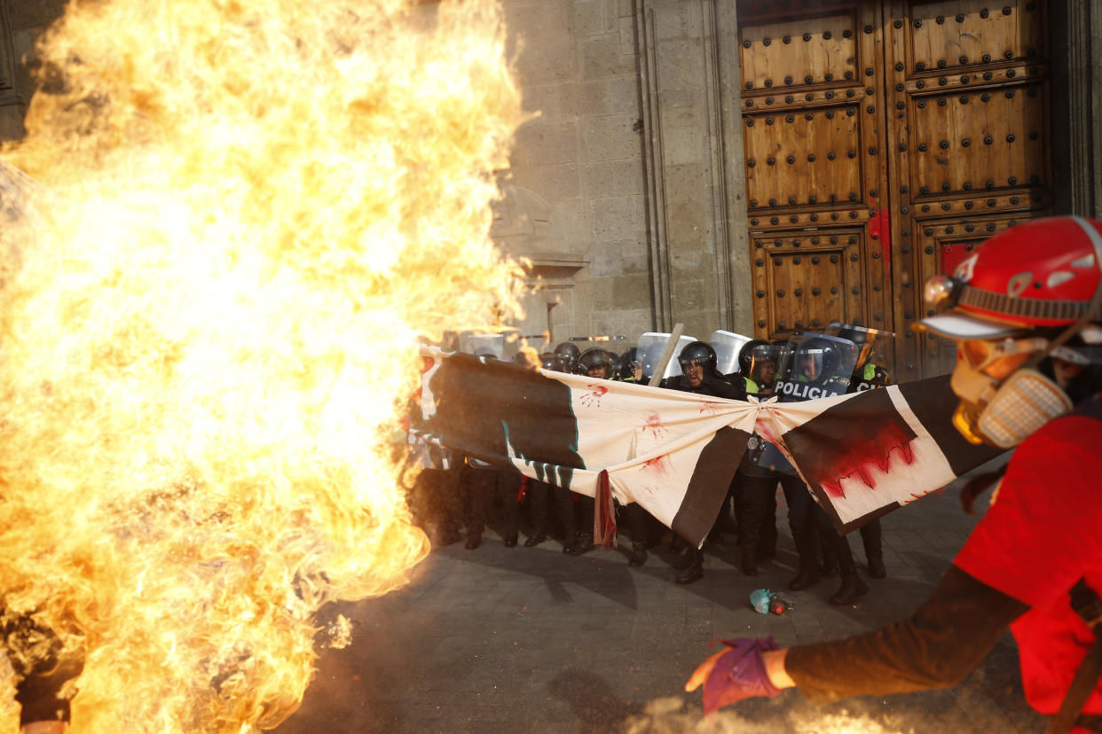 Policías antimotines mantienen la línea mientras son atacados con bombas incendiarias en la puerta del Palacio Nacional, durante una marcha del Día Internacional de la Mujer en la plaza principal de Ciudad de México, el Zócalo, el domingo 8 de marzo de 2020. (AP Foto/Rebecca Blackwell)