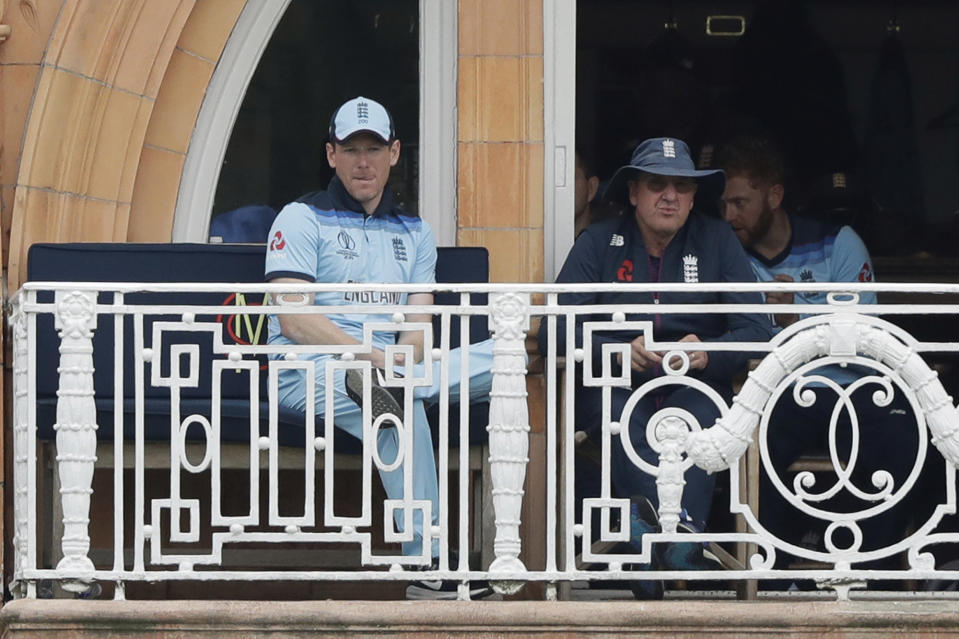 England captain Eoin Morgan, left, and England coach Trevor Bayliss sit on their team's balcony after Morgan was out for four runs during the Cricket World Cup match between England and Australia at Lord's cricket ground in London, Tuesday, June 25, 2019. (AP Photo/Matt Dunham)