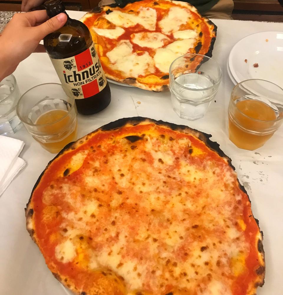 Two round pizzas on a white table and a hand holding an Ichnusa beer bottle