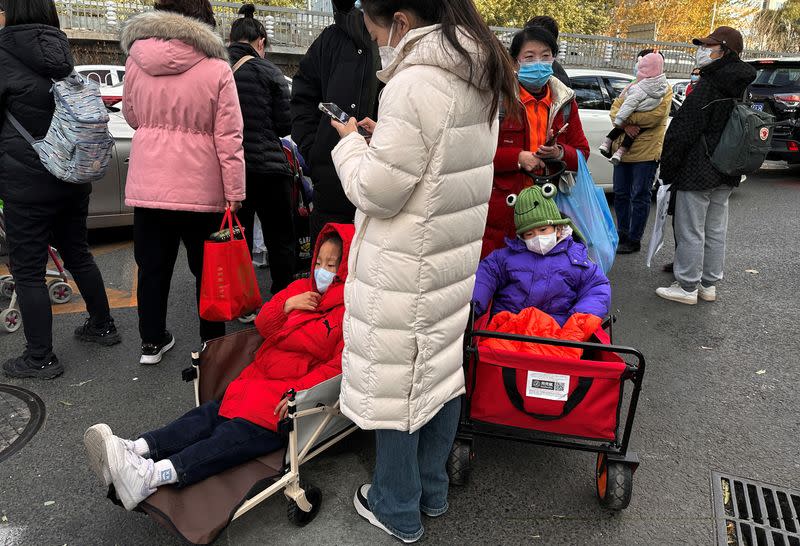 People stand next to children sitting in camping carts as they wait for their rides outside a children's hospital in Beijing