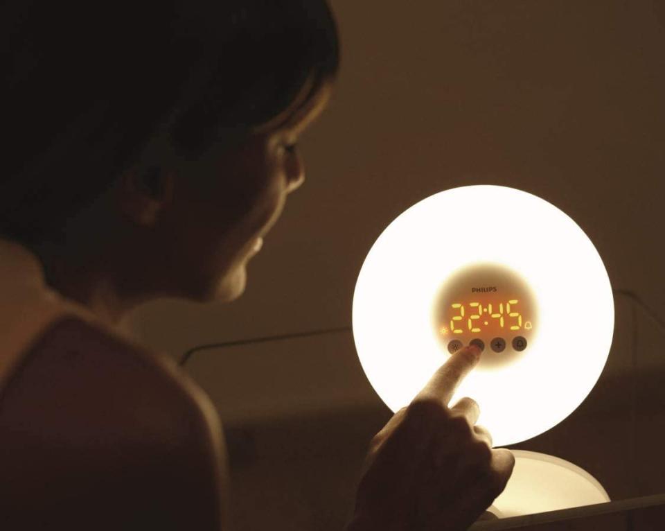 Dark image of woman adjusting brightness of Philips HF3500/60 SmartSleep Wake-Up Light Therapy Alarm Clock. 