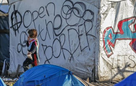 A young migrant walks past graffiti reading "Open the border" in a muddy field at a camp of makeshift shelters for migrants and asylum-seekers from Iraq, Kurdistan, Iran and Syria, called the Grande Synthe jungle, near Dunkirk, France, January 25, 2016. REUTERS/Yves Herman