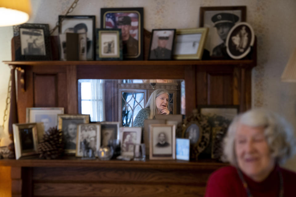 Nancy Rose, center in mirror, speaks with her mother, Amy Russell, right, who both contracted COVID-19 in 2021, in their dining room surrounded by pictures of relatives and family, Tuesday, Jan. 25, 2022, in Port Jefferson, N.Y. More than a third of COVID-19 survivors by some estimates develop lingering problems. (AP Photo/John Minchillo)