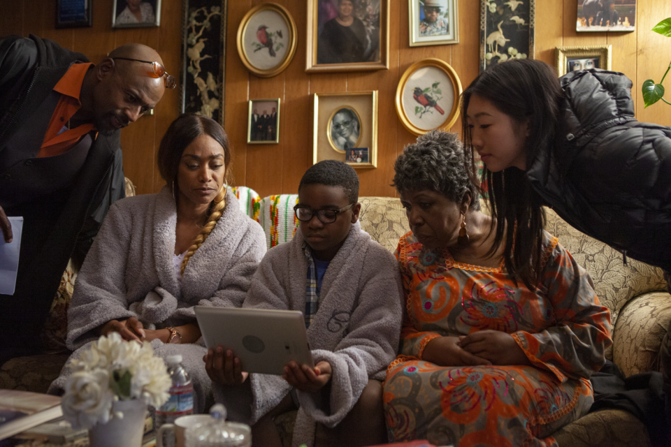 The cast gathers around to watch something on Lil' Eric's tablet.