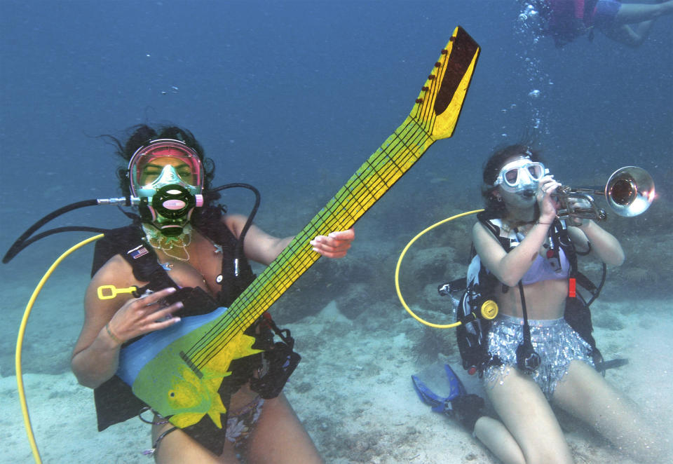 In this photo provided by the Florida Keys News Bureau, Kelly Angel, left, and Kara Norman, right, pretend to play underwater musical instruments, Saturday, July 8, 2023, at the Lower Keys Underwater Music Festival in the Florida Keys National Marine Sanctuary near Big Pine Key, Fla. Several hundred divers and snorkelers submerged along a portion of the continental United States' only living coral barrier reef to listen to a local radio station's four-hour broadcast, piped beneath the sea to promote coral reef preservation. (Frazier Nivens/Florida Keys News Bureau via AP)