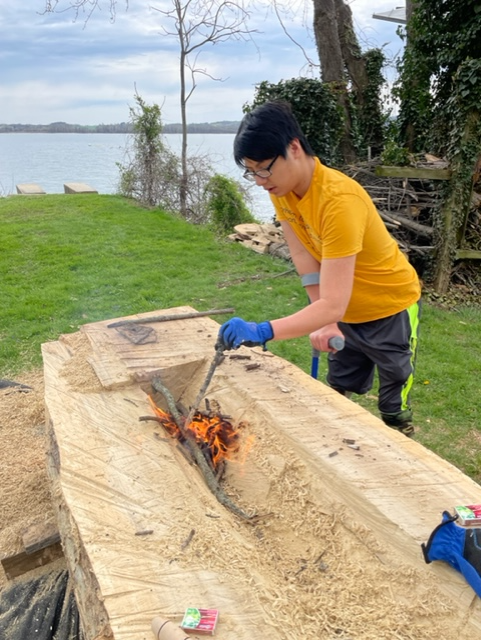 As part of his Eagle Scout project in 2022, Noah Platts ignites a fire to convert a tree trunk into a dugout canoe in the summer of 2022. The flames turned the wood into charcoal, which he scraped off with an adz. The burning of a trunk as part of the process of hollowing out a tree trunk was a practice used by Native Americans to make dugout canoes.
