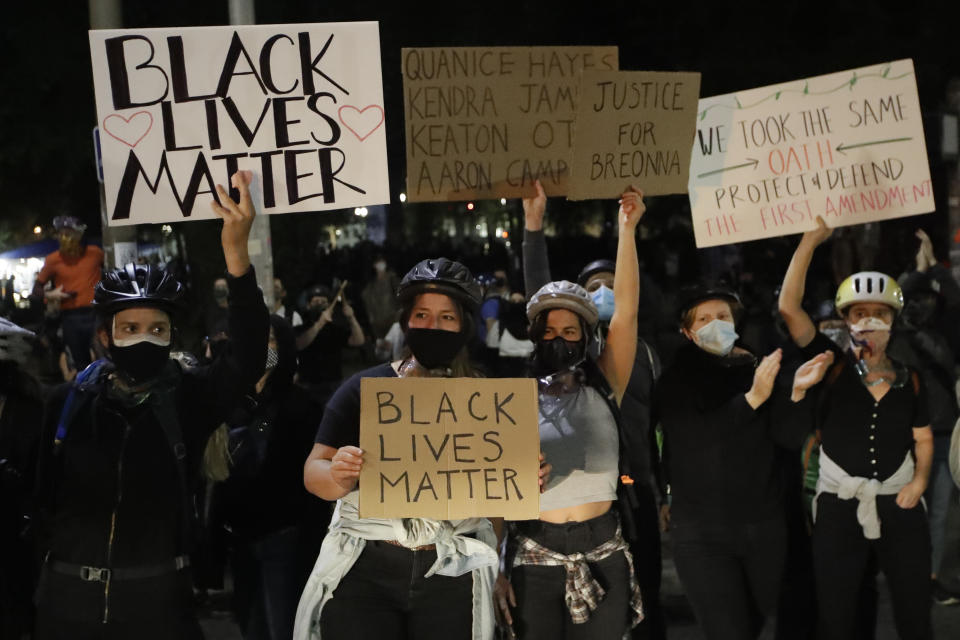 Demonstrators hold signs during a Black Lives Matter protest at the Mark O. Hatfield U.S. Courthouse on Friday, July 24, 2020, in Portland, Ore. On the streets of Portland, a strange armed conflict unfolds night after night. It is raw, frightening and painful on both sides of an iron fence separating the protesters on the outside and federal agents guarding a courthouse inside. This weekend, journalists for The Associated Press spent the weekend both outside, with the protesters, and inside the courthouse, with the federal agents, documenting the fight that has become an unlikely centerpiece of the protest movement gripping America. (AP Photo/Marcio Jose Sanchez)