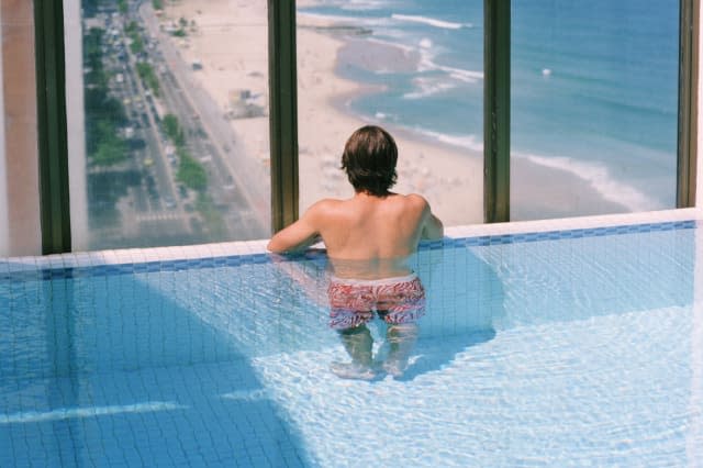 Young man standing in pool, looking through window, rear view, elevated view