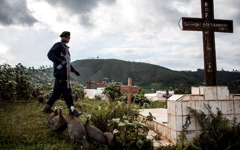 A police officer escorts the coffins containing two victims of Ebola. he Red Cross warned that critical underfunding could force it to cut vital work - Credit: JOHN WESSELS/AFP